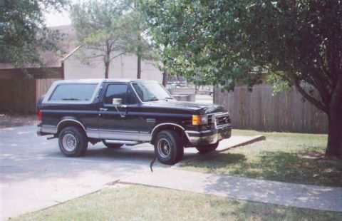 1990 Ford Bronco - This 1990 Ford Bronco is parked outdoors near a tree and a building.