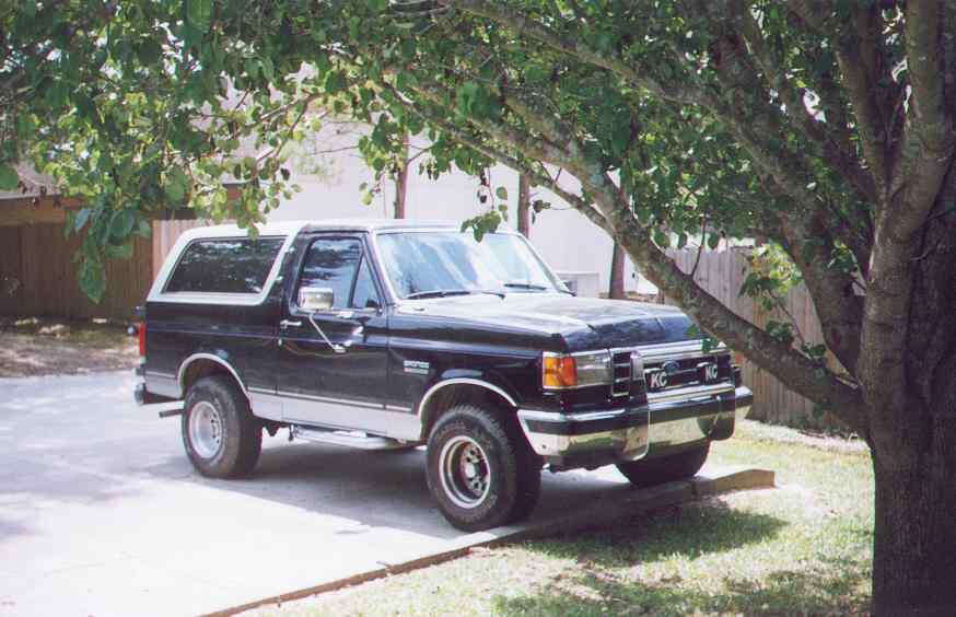 Black and silver Ford Bronco parked under a tree, front quarter view