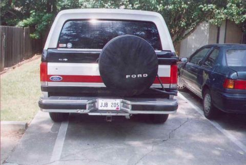 1990 Ford Bronco - The rear of a 1990 Ford Bronco is visible, a spare tire on the back and a red stripe accent.