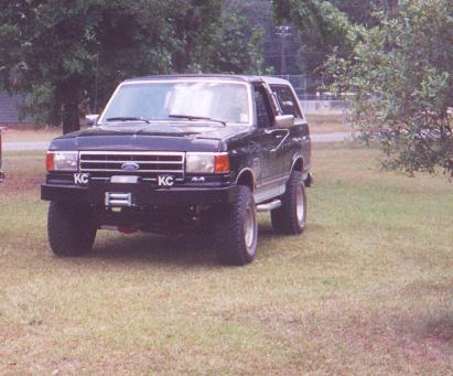 1990 Ford Bronco - This black Ford Bronco is parked on a grassy lawn with trees in the background.