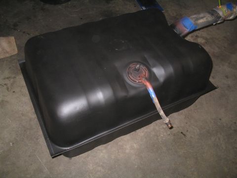 1979 Ford Bronco - A black fuel tank with a hose connected to its filler neck sits on a concrete floor.