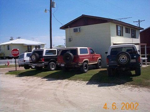 1990 Ford Bronco - Three SUVs, including two Ford Broncos, are parked in front of a building on a sunny day.