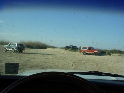 1990 Ford Bronco - Three SUVs are parked on sand dunes on a sunny day.