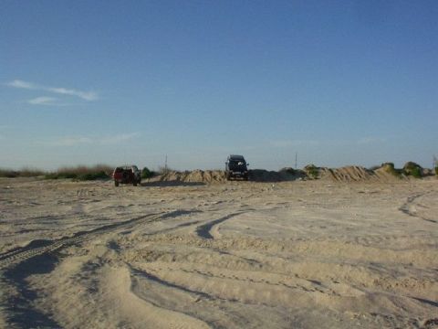 1990 Ford Bronco - Two SUVs are parked on a sandy area under a clear blue sky.