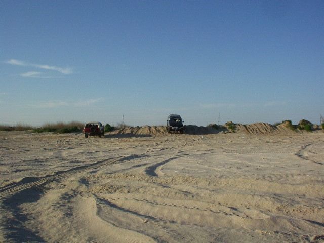 two SUVs parked on a sandy area with tire tracks in the foreground