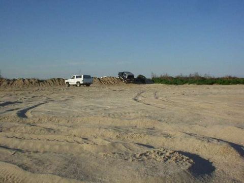 1990 Ford Bronco - Two SUVs are visible on a sandy landscape with tire tracks in the foreground.