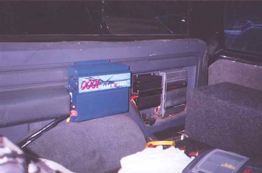 Car audio system with amplifiers and subwoofer box inside a vehicle.