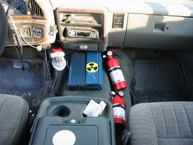 Interior of a 1990 Ford Bronco showing dashboard, center console, and floor mats with fire extinguishers and electronics.