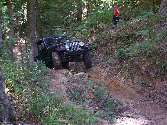 Black Jeep Wrangler driving down a steep, dirt trail in a forest.