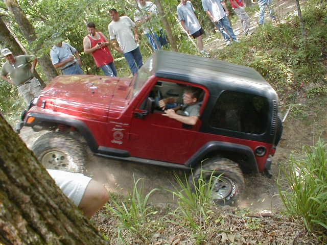 Red Jeep Wrangler driving on a dirt trail with people watching.