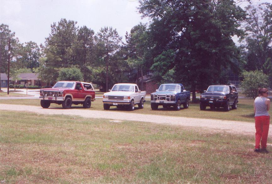 Four Ford trucks and SUVs parked in a line, with a woman standing to the right.
