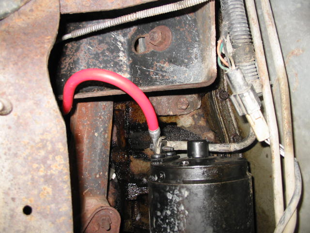 Red cable connected to starter motor assembly on a vehicle.