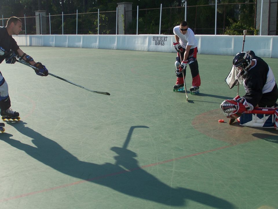 Three people playing roller hockey on an outdoor court.