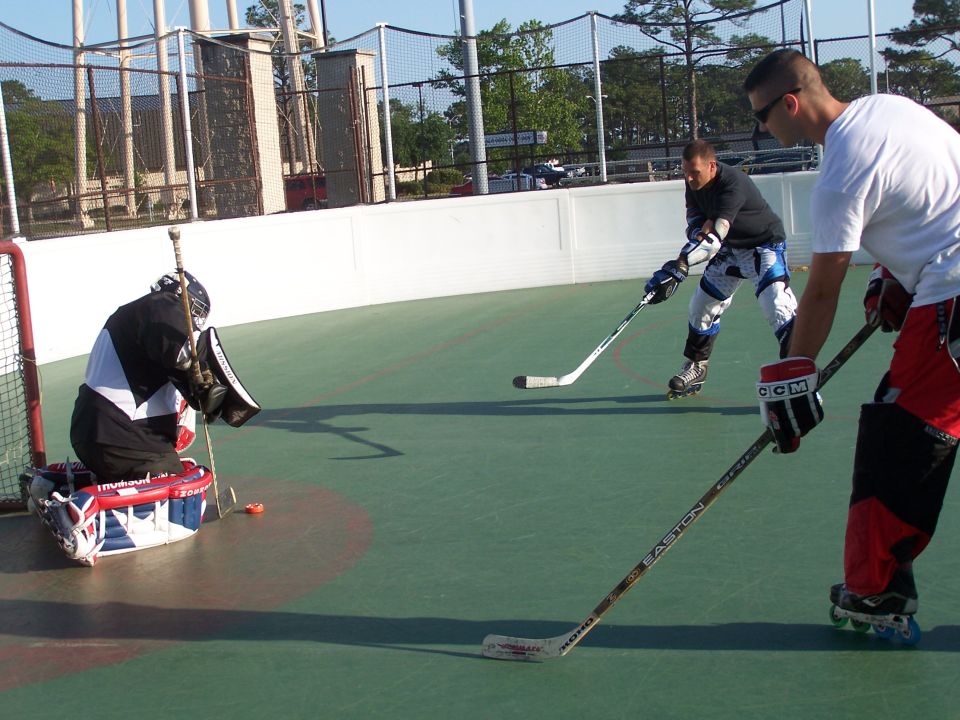 Three people playing roller hockey on an outdoor court.