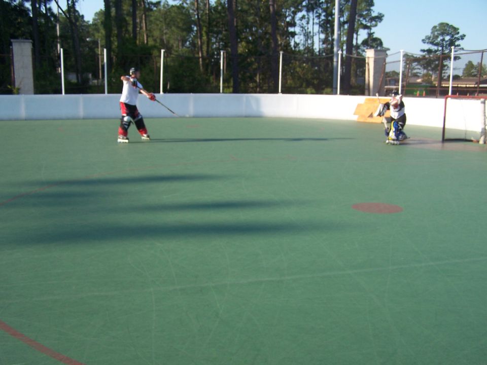 Two people playing inline hockey on a green court