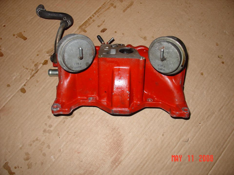 Red automotive intake manifold with two vacuum actuators and a black hose.
