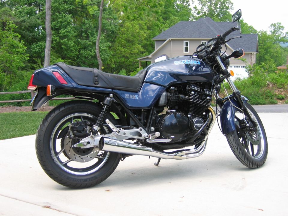 Blue Suzuki motorcycle parked on pavement with a house in the background