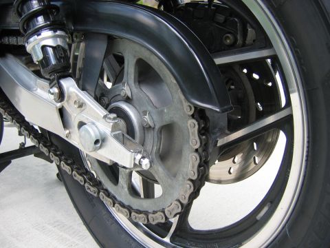 1985 Ford LTD Crown Victoria - Close-up view of a motorcycle's rear wheel, drive chain, and suspension system.