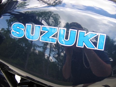 1985 Ford LTD Crown Victoria - A close-up of the SUZUKI logo on a motorcycle's dark blue fuel tank.