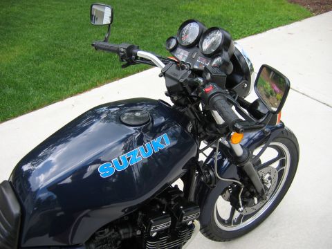 1985 Ford LTD Crown Victoria - A dark blue Suzuki motorcycle is parked on a paved surface next to a grassy area.