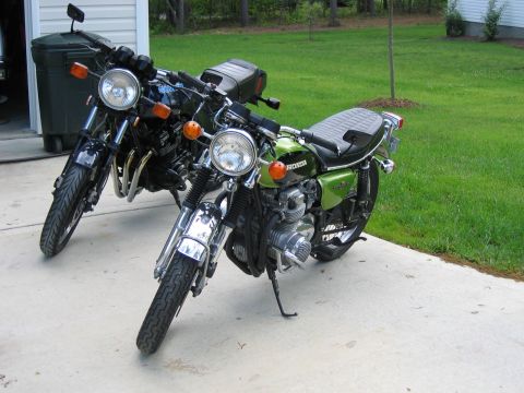 1985 Ford LTD Crown Victoria - Two motorcycles are parked on a concrete driveway next to a trash can and a grassy yard.