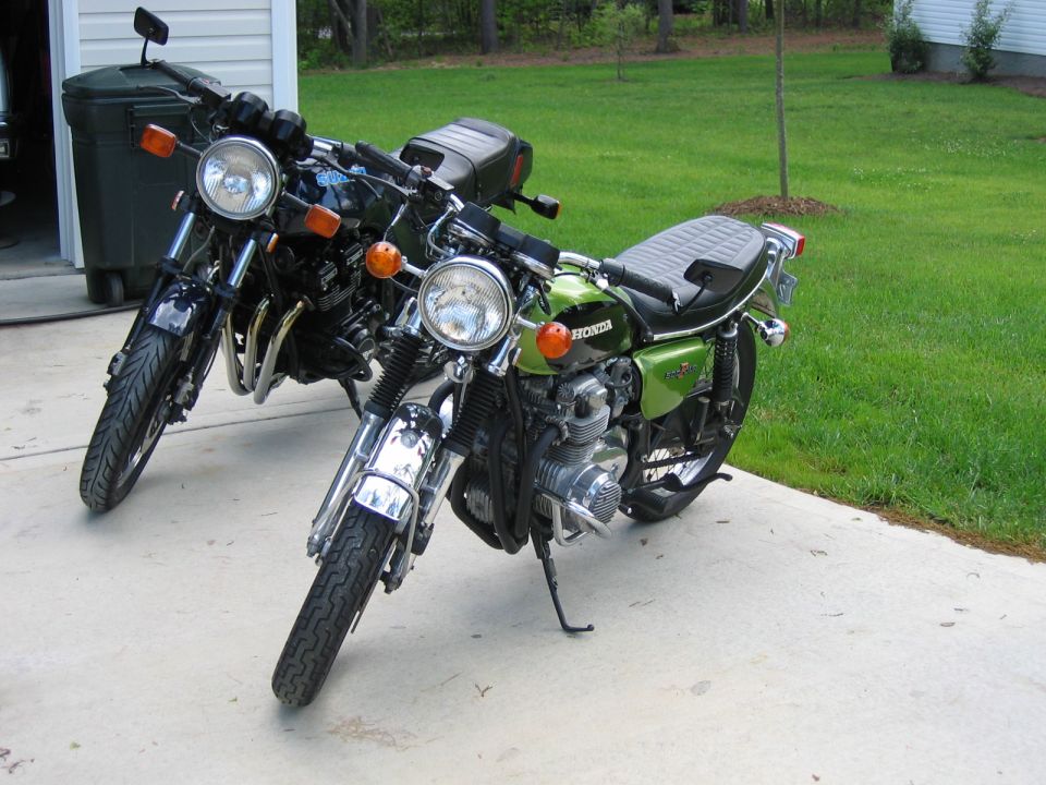 Two motorcycles parked on a concrete driveway, one green and one black. The green motorcycle is in the foreground