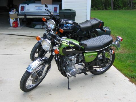 1985 Ford LTD Crown Victoria - Two motorcycles are parked on a concrete driveway in front of a garage.