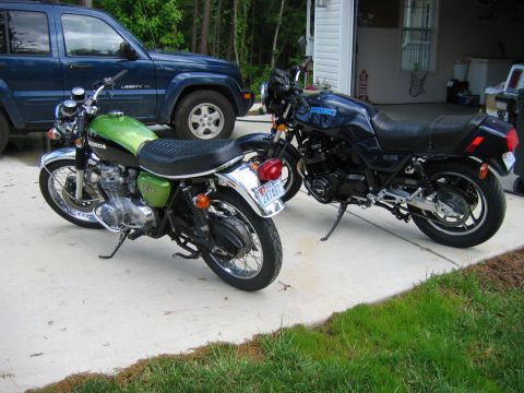 1985 Ford LTD Crown Victoria - Two motorcycles and a blue SUV parked in a driveway next to a garage.