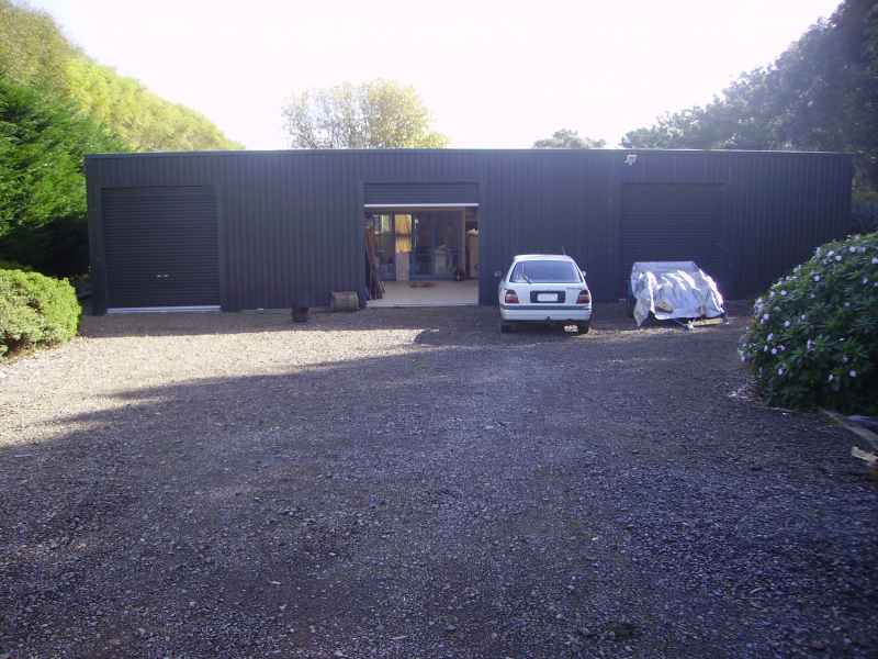 White sedan and tarp-covered car parked at a dark steel workshop on a gravel drive