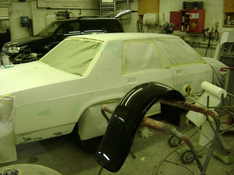 2001 Ford Crown Victoria - A white sedan is being prepped for paint in a body shop, with a black fender on a stand and a 3M cabinet in the background.