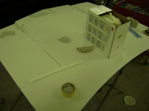2001 Ford Crown Victoria - A car hood is prepared for painting with various automotive repair supplies laid out on its surface.