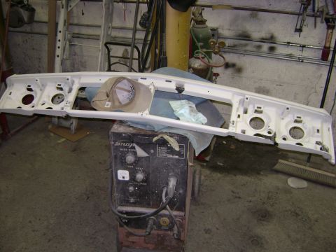 2001 Ford Crown Victoria - A white car front bumper assembly, likely for a sedan, is shown disassembled and resting on a welding machine in a workshop.