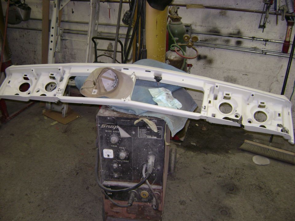 White car front bumper assembly with headlight cutouts, resting on a welding machine