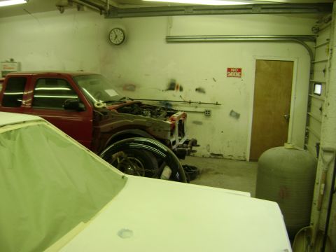 2001 Ford Crown Victoria - A red pickup truck is in a garage with its hood open, next to a white vehicle covered in a tarp.