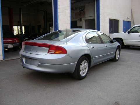 2001 Ford Crown Victoria - A silver sedan is parked outside a garage, with a white pickup truck and a red car visible.
