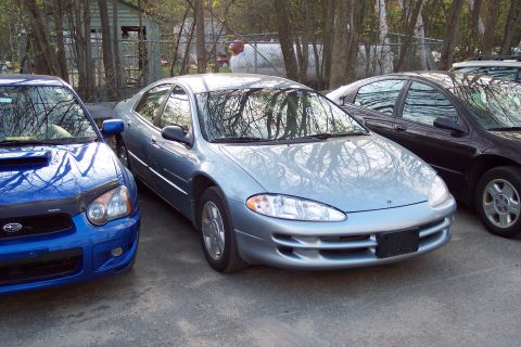 2001 Ford Crown Victoria - Three cars are parked in an outdoor lot. The middle car is a light blue sedan.