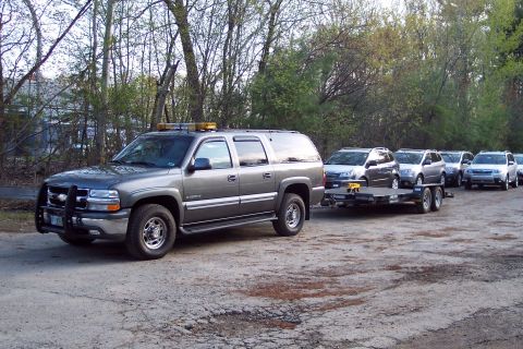 2001 Ford Crown Victoria - A large SUV tows a car trailer, with several other vehicles lined up behind it on a dirt road.
