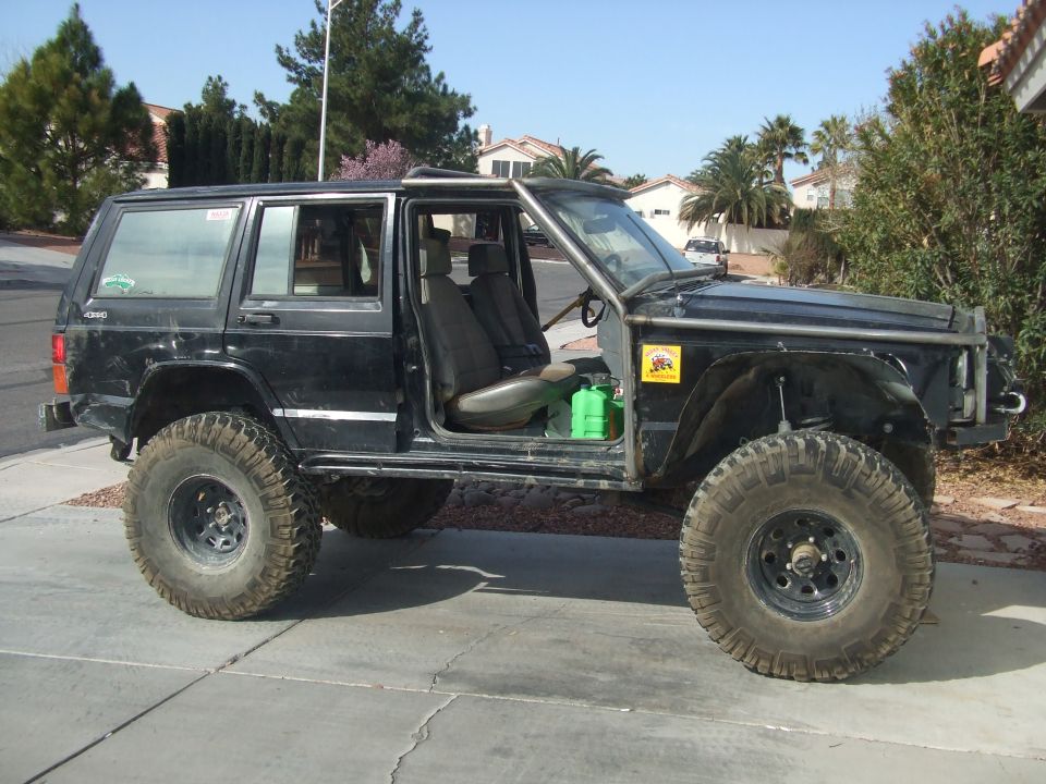 Black Jeep Cherokee with doors removed, roll cage, and large off-road tires parked on a driveway