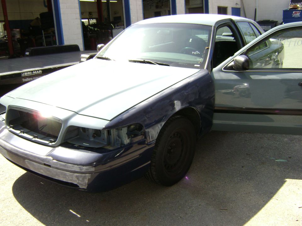 Blue and gray 2001 Ford Crown Victoria with front end damage and open driver's door