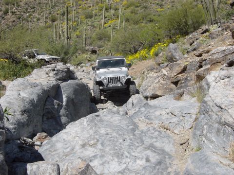 1986 Toyota Hilux - A Jeep Wrangler tackles a challenging off-road course in a desert landscape.