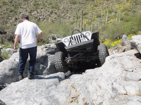 1986 Toyota Hilux - A white Jeep Wrangler is shown off-roading over large rocks in a desert landscape.