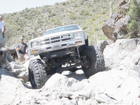 1986 Toyota Hilux - Modified Toyota pickup truck with lifted suspension and oversized tires tackles a challenging rocky trail.