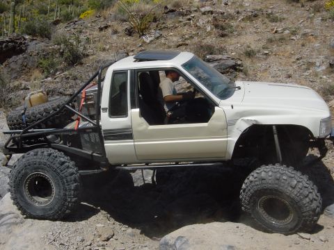 1986 Toyota Hilux - This heavily modified pickup truck navigates a challenging rocky terrain with a driver inside.