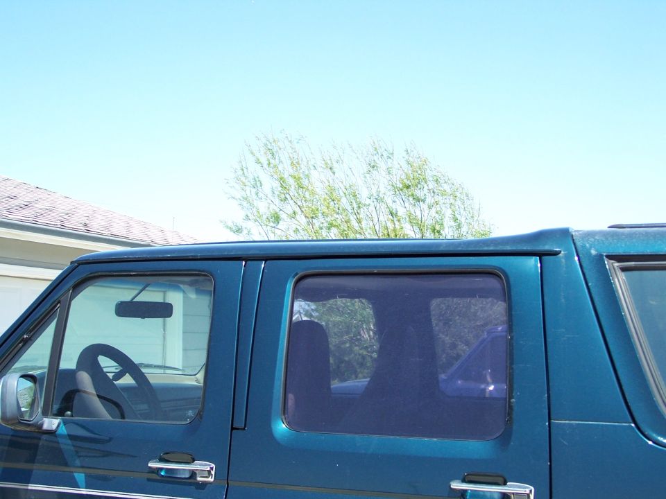 Teal Ford van upper side view showing door glass, rear window and roofline against blue sky