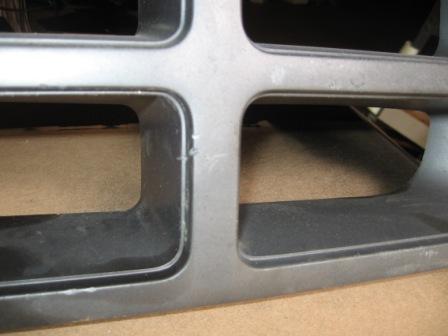 1993 Ford Bronco - Extreme close-up of a gray plastic grille section removed from the vehicle and resting on cardboard, showing the rectangular openings and t…