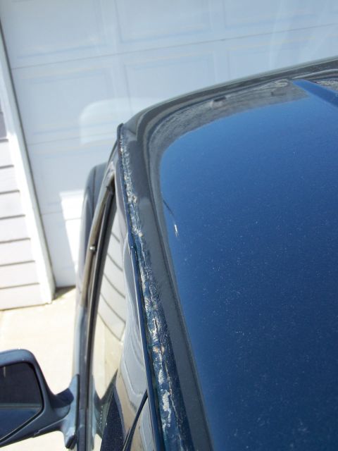 1995 Ford C-150 (Centurion Conversions) - Close-up of the windshield frame on a dark blue pickup truck, showing deteriorated trim around the glass.