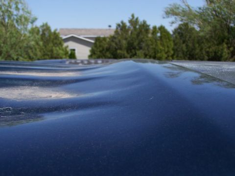 1995 Ford C-150 (Centurion Conversions) - The wavy surface of a dark blue vehicle roof is visible, with a house and trees blurred in the background under a clear sky.