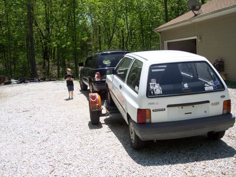 2007 Dodge Durango - A white hatchback is towed by a black SUV in a gravel driveway next to a house.