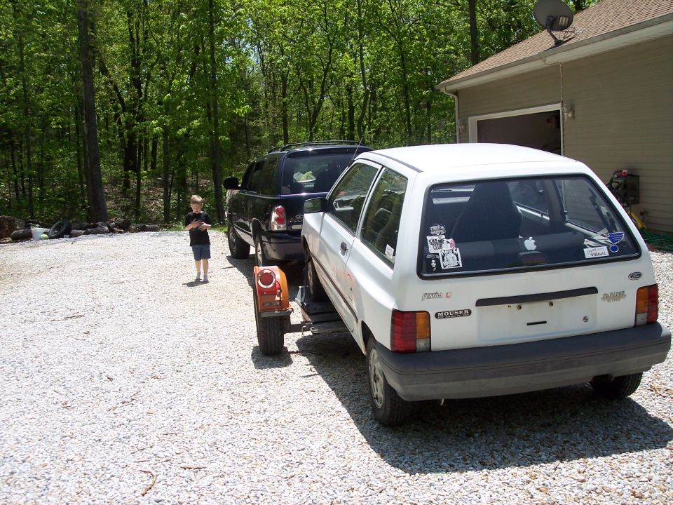 White hatchback car with stickers on rear window, being towed by black SUV