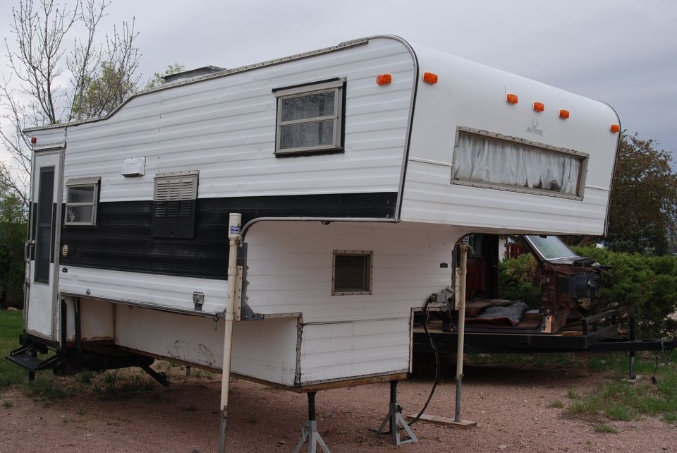 White and black camper on jack stands, with a trailer frame visible underneath